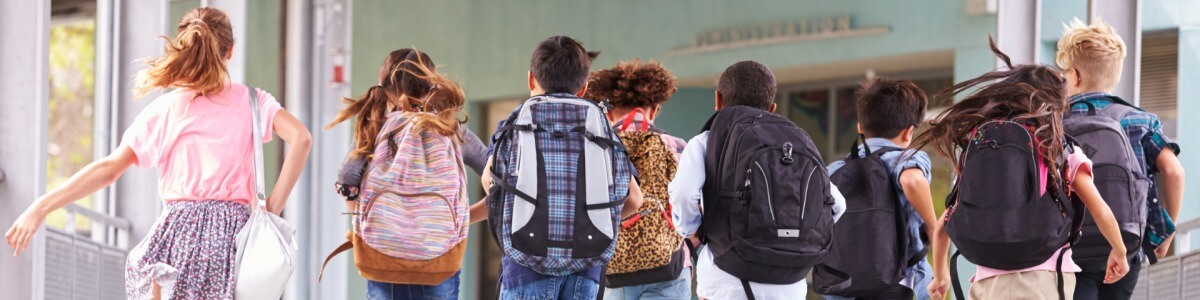 Acht Kinder laufen mit Schulrucksäcken zum Unterricht