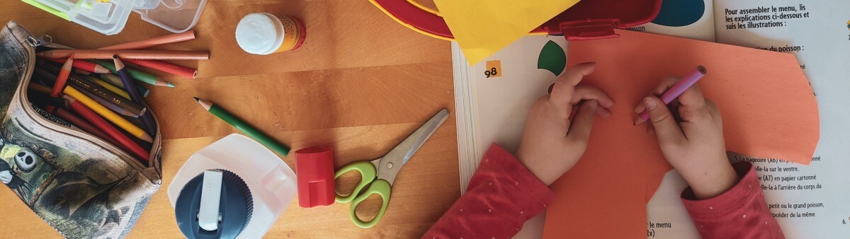 Ein Kind bastelt mit Utensilien wie Schere, Papier, Leim und Farbstiften