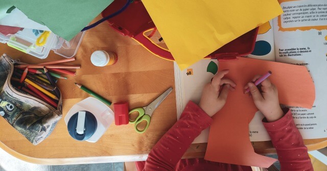 Ein Kind bastelt mit Utensilien wie Schere, Papier, Leim und Farbstiften