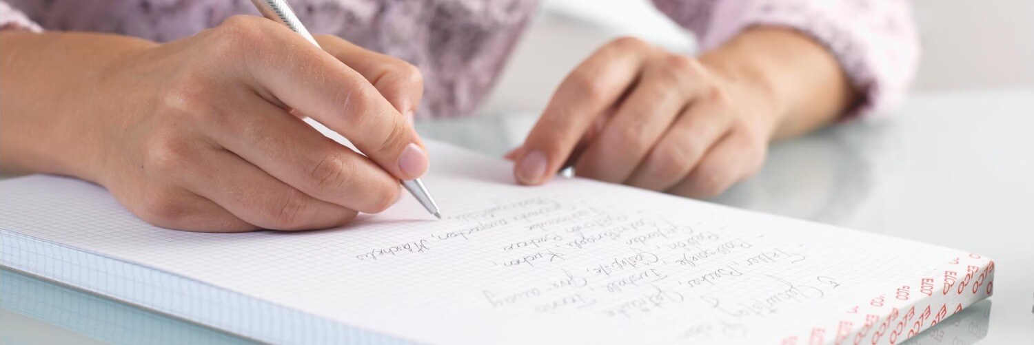 Frau schreibt mit Kugelschreiber auf karierten A4 Notizblock von Elco