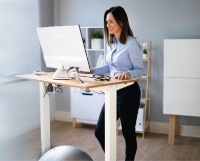 Eine Frau steht an einem ergonomischen höhenverstellbaren Schreibtisch