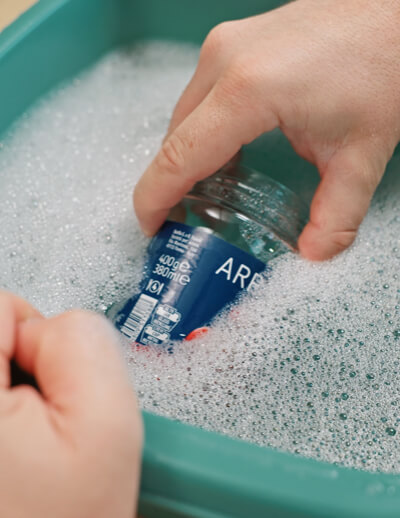 Glas mit Etikette wird in Becken mit Wasser uns Spülbecken gelegt