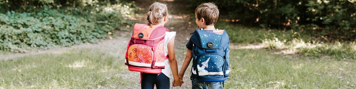 Zwei Kinder laufen mit Rucksäcken zur Schule
