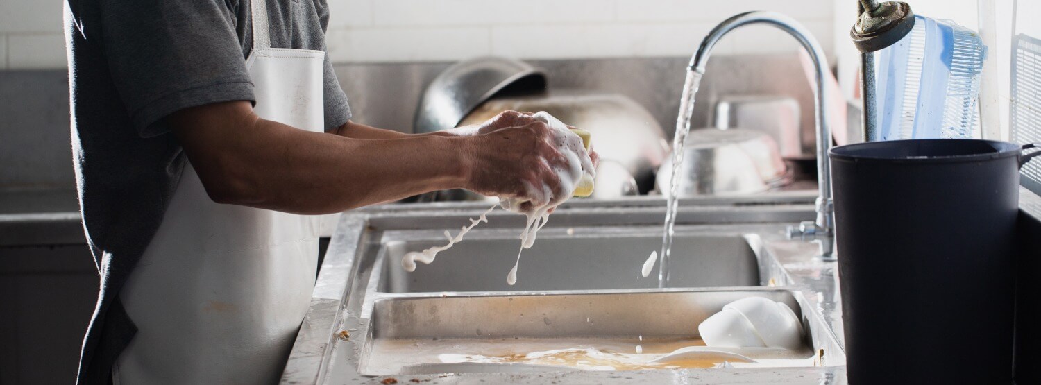 Mann wäscht schmutziges Geschirr mit Geschirrspülmittel und Schwamm