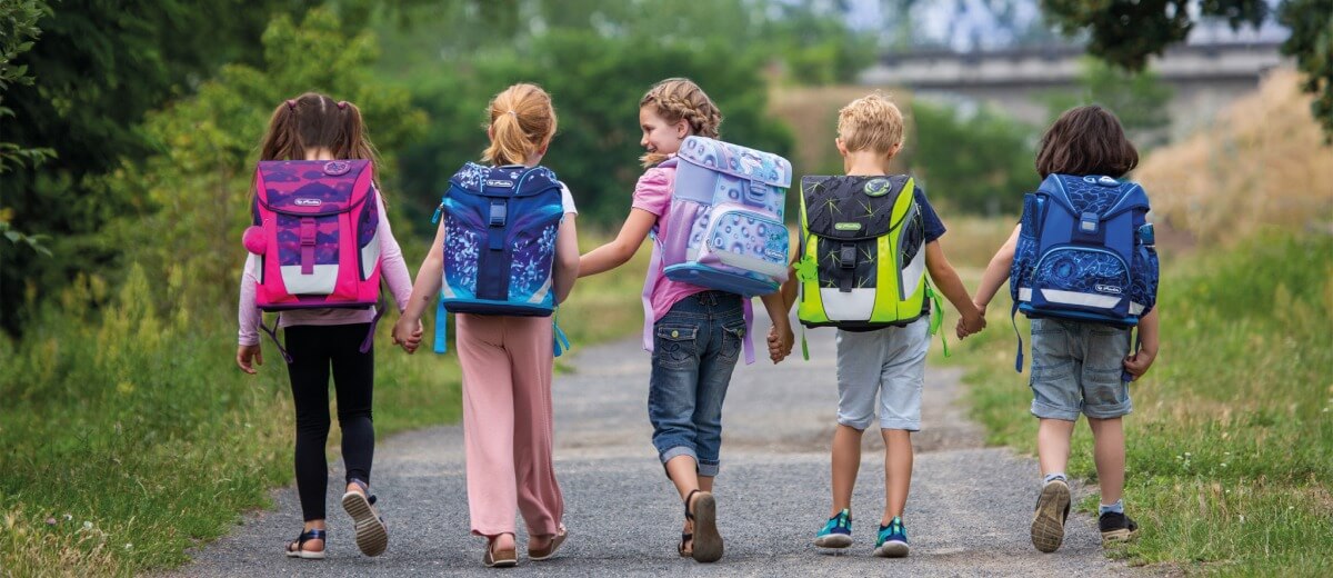 Kinder laufen zusammen mit Schulthek am Rücken zur Schule