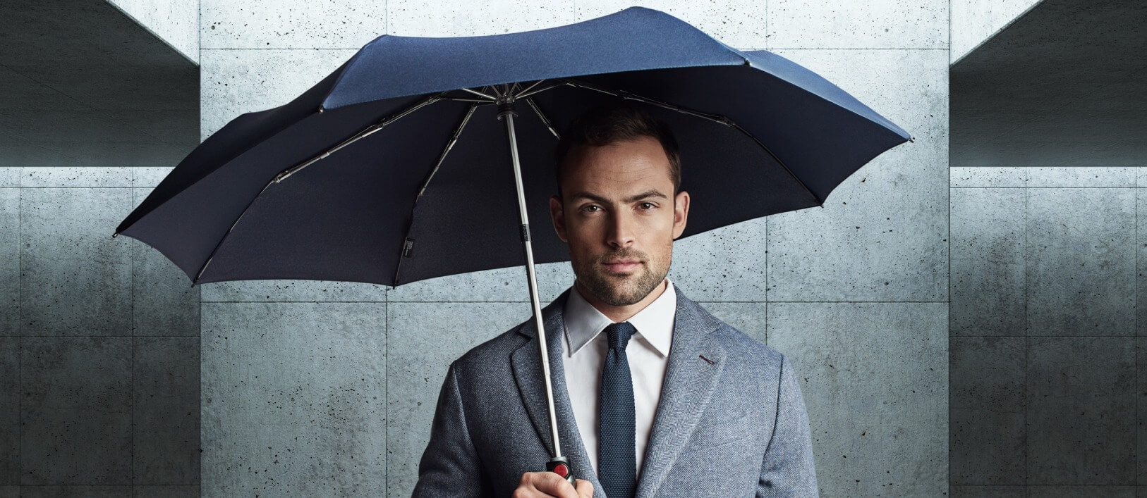 Mann im Anzug mit navy-blauem Knirps Regenschirm
