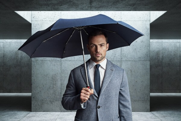 Mann im Anzug mit navy-blauem Knirps Regenschirm