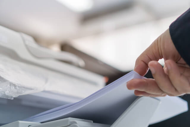 Eine Person nimmt einen Stapel Kopierpapier aus einem Drucker