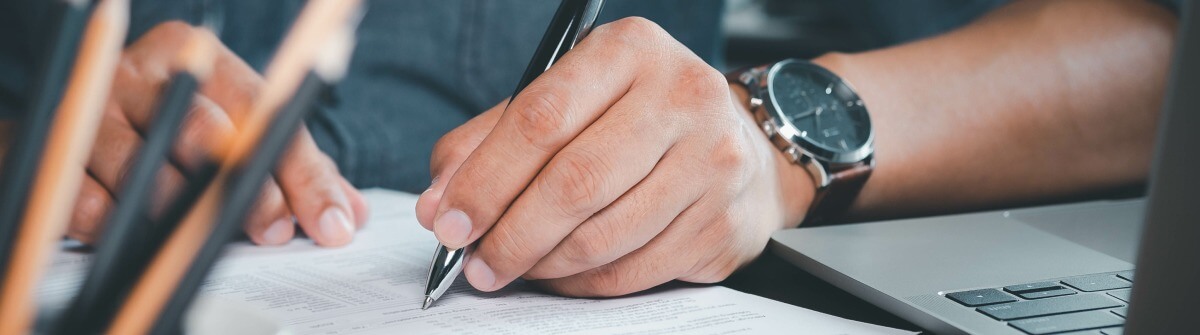 Ein Mann schreibt mit einem Kugelschreiber auf ein Blatt Papier