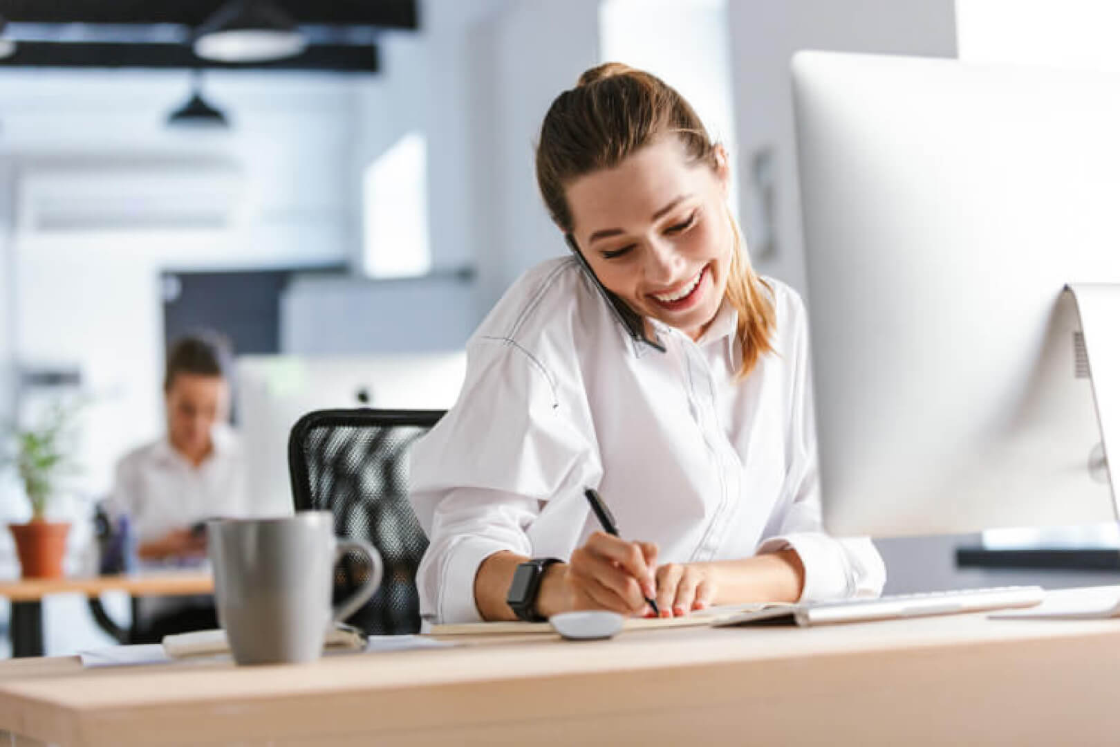Junge Frau telefoniert im Büro und macht notizen