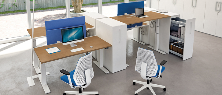 Büromöbelprogramm Linus+ mit 4 Tischen in 2 Reihen gegenübergestellt und auf unterschiedliche Höhen eingestellt. Sie sind an der Stirnseite mit blauen Akustikpaneelen, die an den Tischen angebracht sind und seitlich mit hohen Auszugsschränken voneinander abgetrennt.