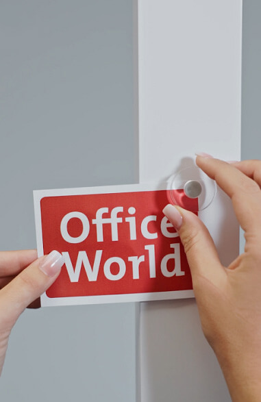 Person haftet Office World Logo mit einem Magnet an eine Stehleuchte