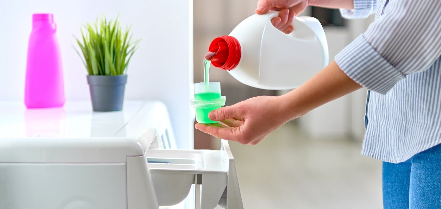 Frau befüllt Waschmaschine mit Flüssig-Waschmittel