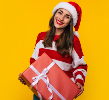 Frau mit Weihnachtsmann-Mütze hält Weihnachtsgeschenk und lächelt