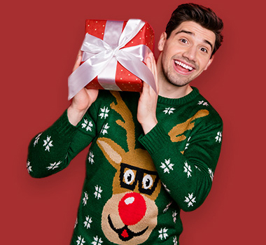 Mann in Weihnachtspullover hält Weihnachtsgeschenk und lächelt