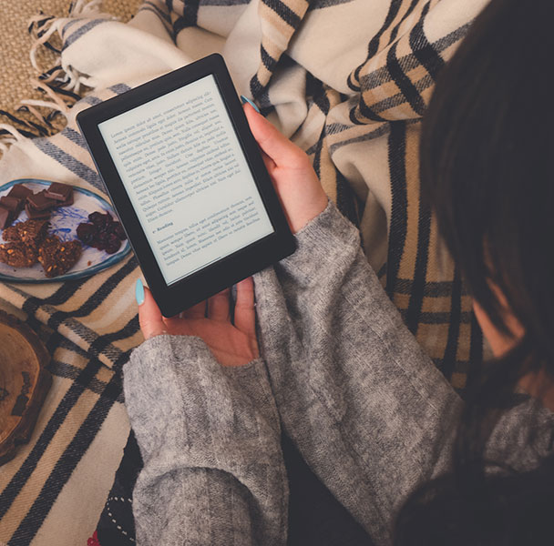 Eine Frau liest gemütlich etwas auf ihrem E-Book Reader