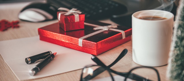 Verpackte Geschenke liegen auf einem Schreibtisch zwischen einer Kaffeetasse, einer Tastatur und einem Kugelschreiber