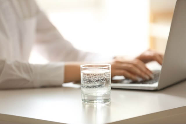 Ein Glas Minerwasser im Büro neben einem Laptop
