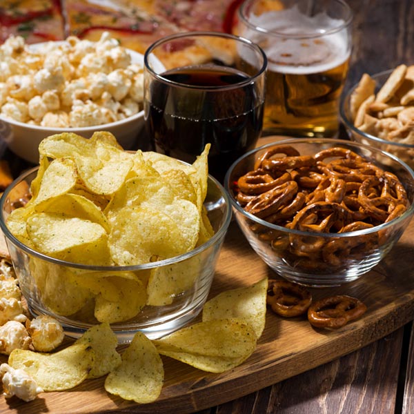 Chips, Salzbrezeln und Popcorn in Schüsselchen und Cola und Rivella Gläsern auf einem Tisch angerichtet