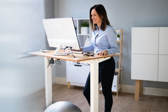 Eine Frau steht an einem ergonomischen höhenverstellbaren Schreibtisch