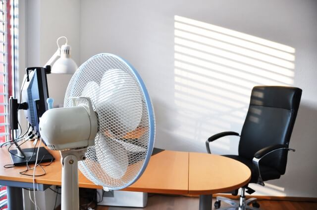 Ein Ventilatorsteht vor einem Büro-Arbeitsplatz